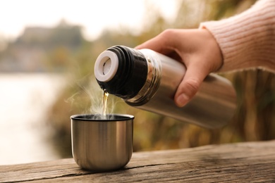 Woman pouring drink from thermos into cap on wooden pier near river, closeup