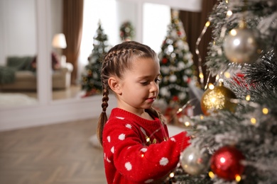 Adorable little child decorating Christmas tree at home