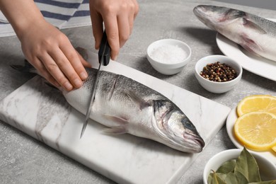 Photo of Woman cutting fresh raw sea bass fish at light gray table, closeup