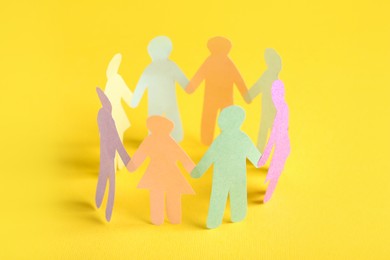 Many different paper human figures standing in circle on yellow background. Diversity and inclusion concept
