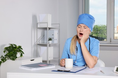 Tired young doctor yawning at workplace in office