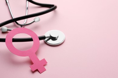 Photo of Female gender sign and stethoscope on pink background, closeup. Space for text