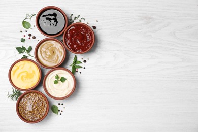 Many different sauces and herbs on white wooden table, flat lay. Space for text