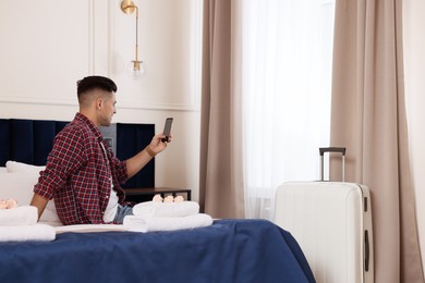 Handsome man using smartphone on bed in hotel room