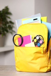 Yellow backpack with different school stationery on table indoors