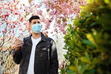 Man with pills and protective mask near blossoming tree outdoors. Seasonal pollen allergy