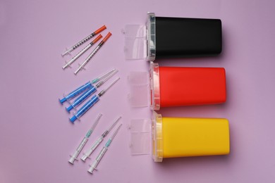 Disposable syringes with needles and sharps containers on violet background, flat lay