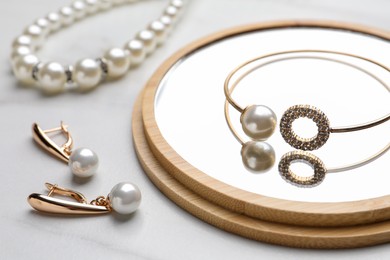 Elegant necklace, bracelet and earrings with pearls on white marble table, closeup