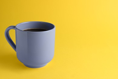 Grey mug of freshly brewed hot coffee on yellow background, space for text