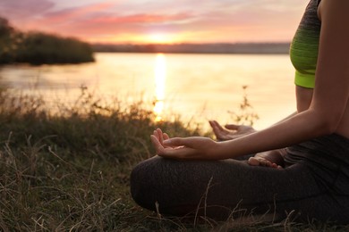 Woman meditating near river at sunset, closeup. Space for text