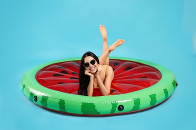 Young woman in stylish sunglasses on inflatable mattress against light blue background