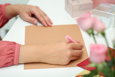 Young woman writing message in greeting card at white table, closeup