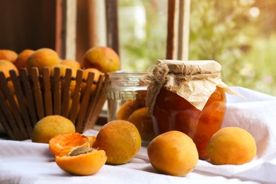 Jar of delicious jam and fresh ripe apricots on tablecloth indoors. Fruit preserve