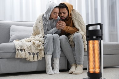Young couple getting warm near electric heater at home