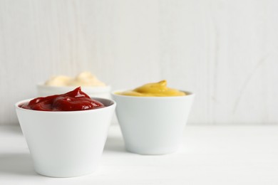 Ketchup, mustard and mayonnaise in bowls on white table, space for text