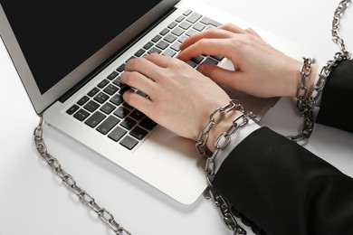 Photo of Man with chained hands typing on laptop against white background, closeup. Internet addiction