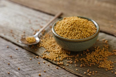 Photo of Bowl and spoon of mustard seeds on wooden table, closeup. Space for text