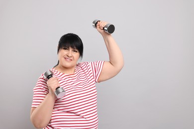 Happy overweight mature woman doing exercise with dumbbells on grey background. Space for text