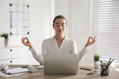 Young businesswoman meditating at workplace. Stress relief exercise