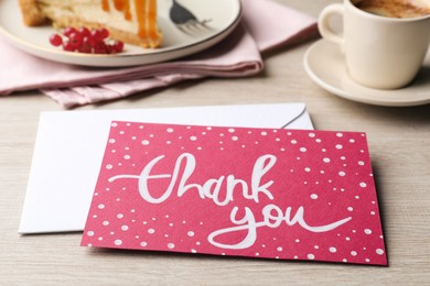 Photo of Card with phrase Thank You, cheesecake and coffee on light wooden table