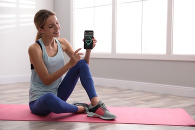 Young woman showing smartphone with fitness app indoors. Space for text
