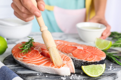 Woman marinating fresh raw salmon at table, closeup. Fish delicacy
