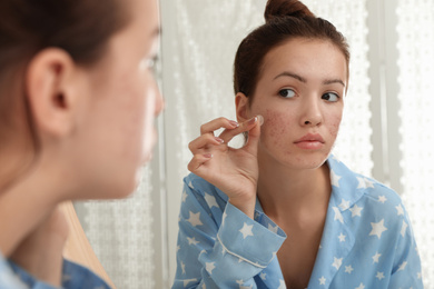 Teen girl applying acne healing patch near mirror in bathroom