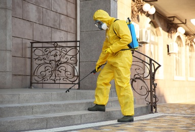 Person in hazmat suit disinfecting stairs with sprayer outdoors. Surface treatment during coronavirus pandemic