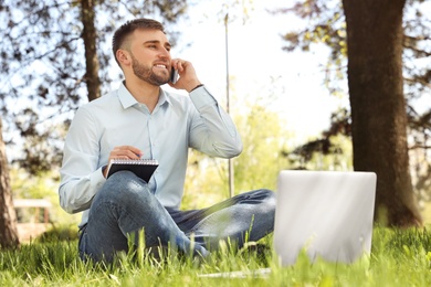 Happy young man with laptop talking on phone in park 