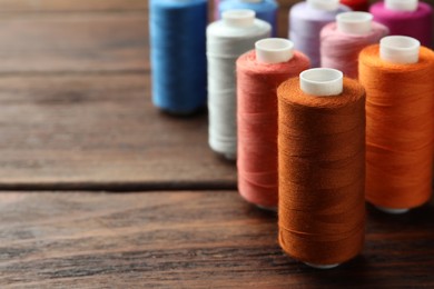 Photo of Different colorful sewing threads on wooden table, closeup. Space for text
