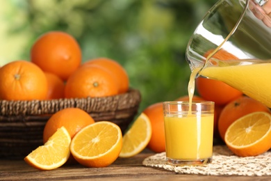 Pouring delicious orange juice into glass at wooden table against blurred background, closeup