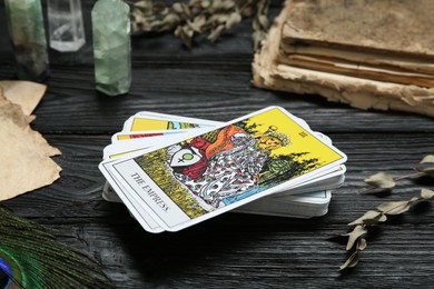 Tarot cards, old book, crystals and peacock feather on black wooden table, closeup