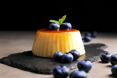 Photo of Delicious caramel pudding with blueberries and mint on grey table against black background, closeup