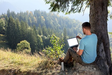 Photo of Man working on laptop outdoors surrounded by beautiful nature, back view