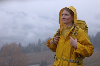 Young woman in raincoat enjoying mountain landscape under rain