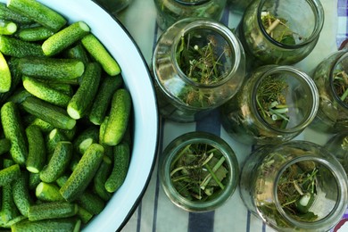 Glass jars with different herbs and fresh cucumbers on table, flat lay. Pickling vegetables