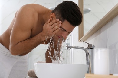 Handsome man washing face over sink in bathroom