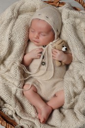 Adorable newborn baby with toy bear sleeping in wicker basket, top view