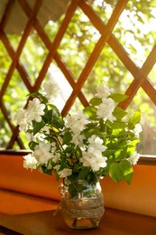 Bouquet of beautiful jasmine flowers in glass vase on wooden table indoors