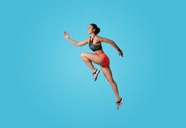 Athletic young woman running on light blue background, side view