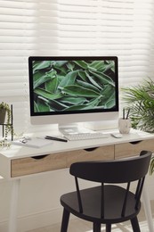 Comfortable workplace with modern computer and green plant in room. Interior design