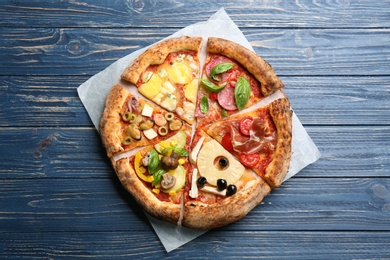 Slices of different pizzas on blue wooden table, top view