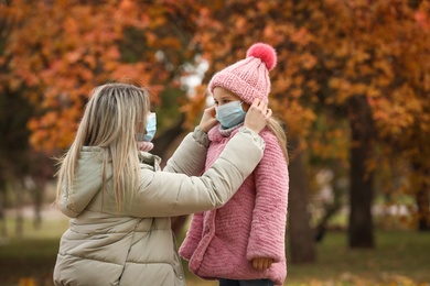 Photo of Mother and daughter in medical masks outdoors on autumn day. Protective measures during coronavirus quarantine