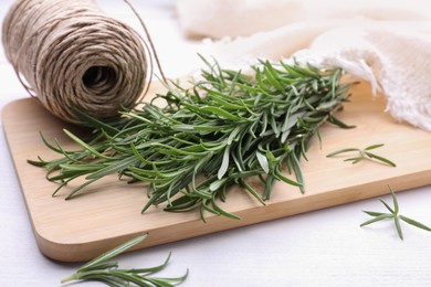 Fresh green rosemary twigs and twine on white wooden table, closeup