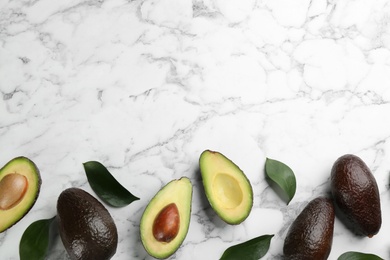 Whole and cut avocados with green leaves on white marble table, flat lay. Space for text