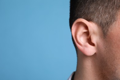 Man on light blue background, closeup of ear. Space for text