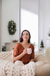 Photo of Woman with hot drink resting in comfortable papasan chair at home