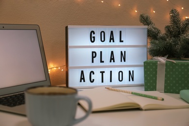 Light box with words Goal, Plan, Action near laptop and gift on table