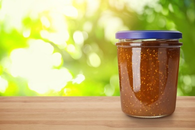 Jar of fig jam on wooden table against blurred background, space for text