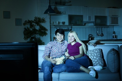 Photo of Young couple with bowl of popcorn watching TV on sofa at night